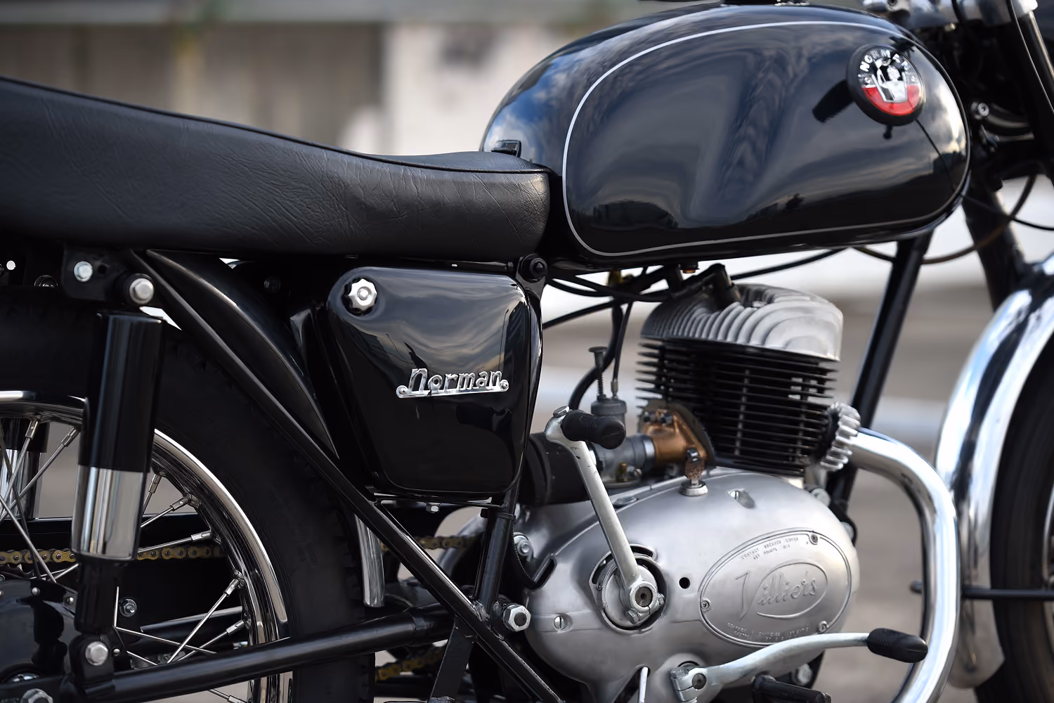 Close-up of a classic black Norman motorcycle engine and seat with chrome and metallic details.
