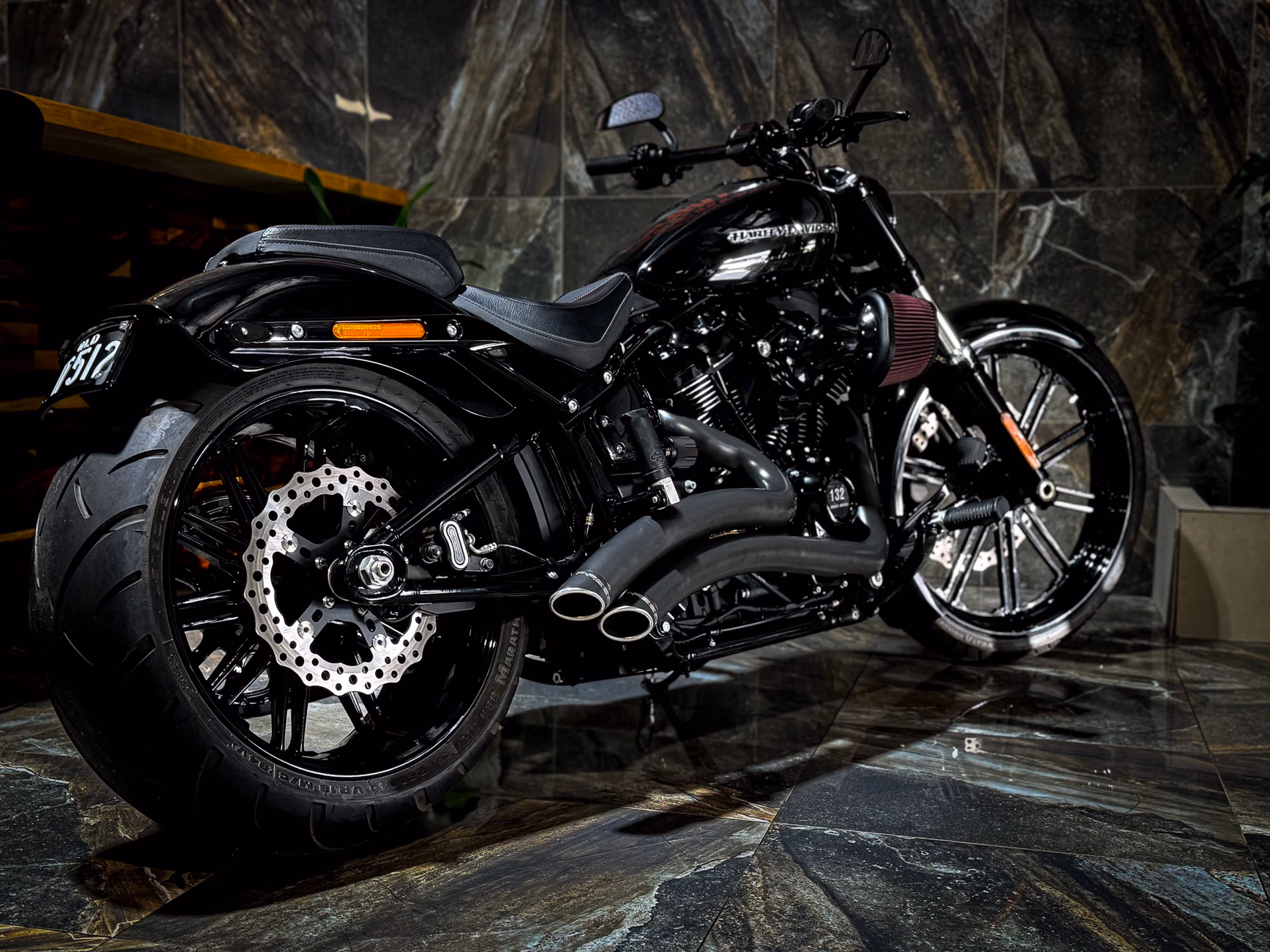 Black Harley-Davidson motorcycle with large rear tire and dual exhausts on marble floor.