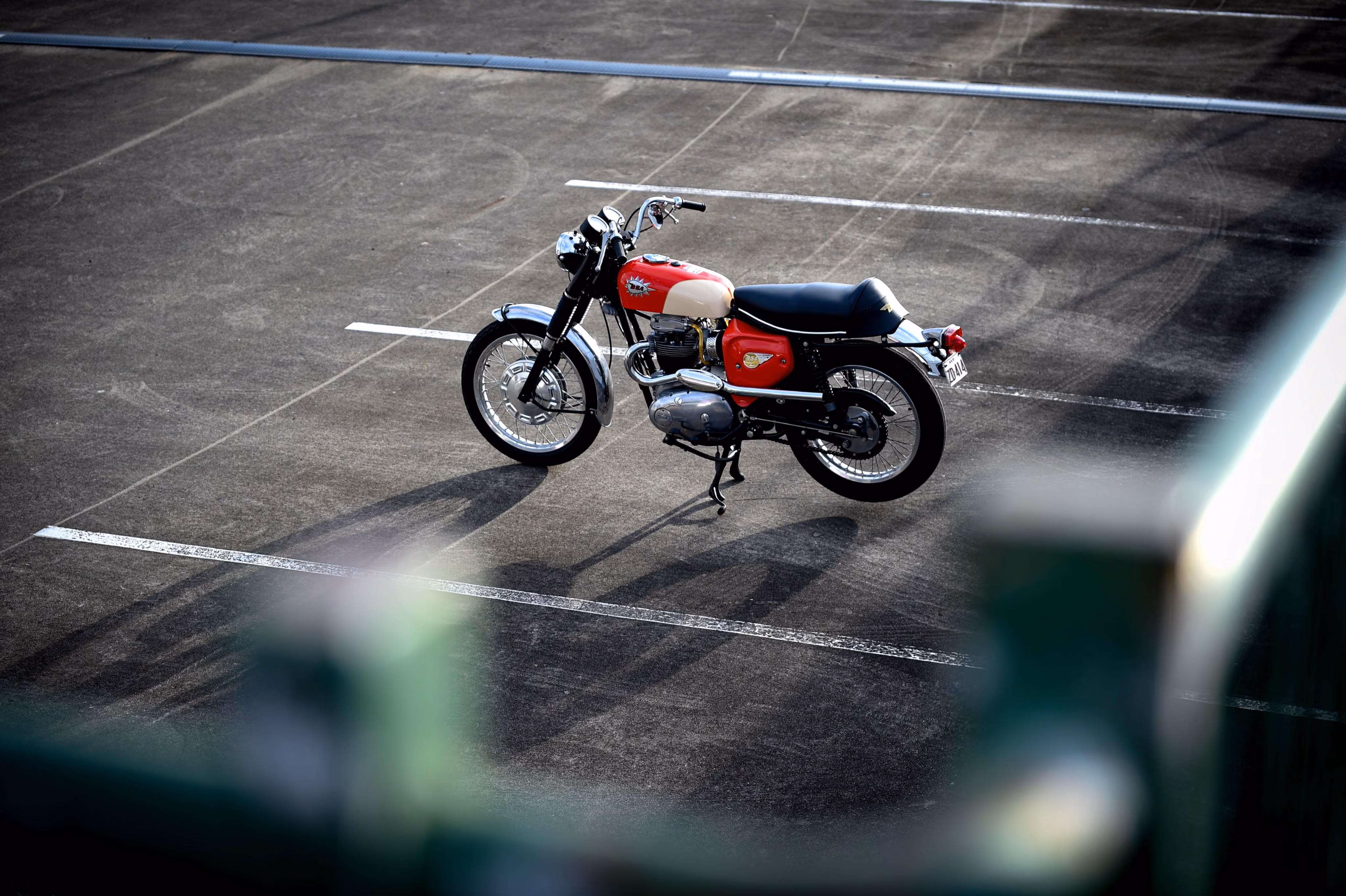 Red and white vintage motorcycle parked in an empty outdoor lot casting a long shadow.