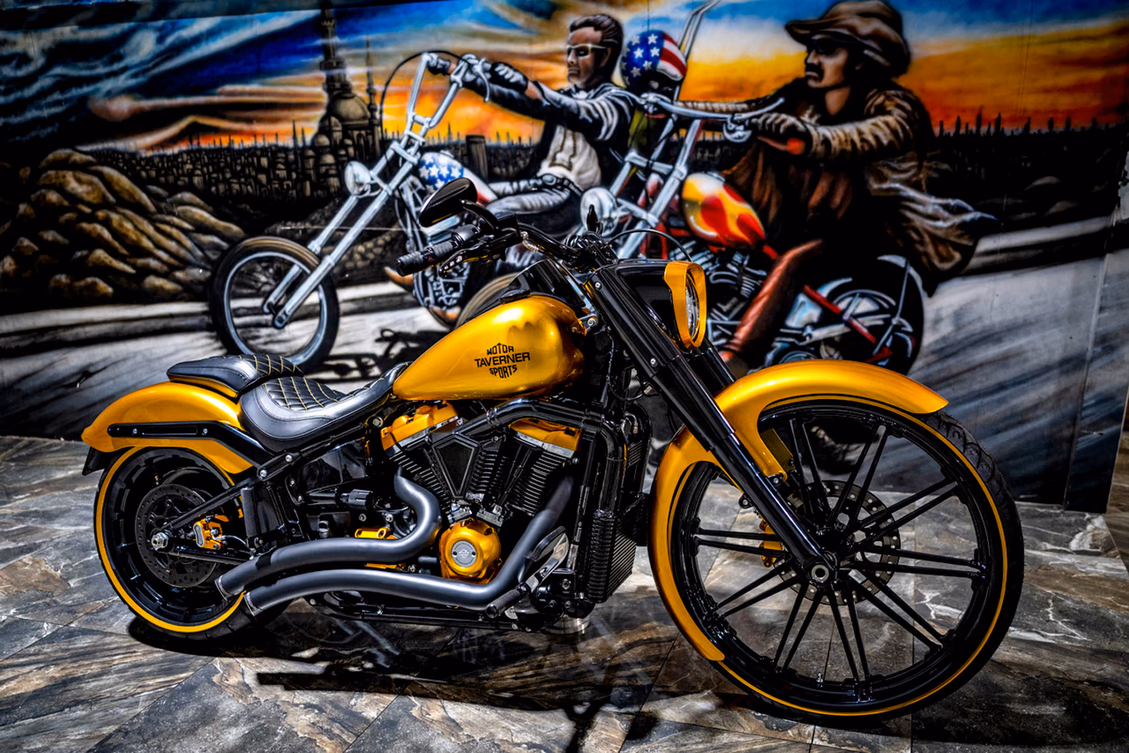 Custom yellow and black motorcycle parked indoors with a mural of two bikers riding at sunset.