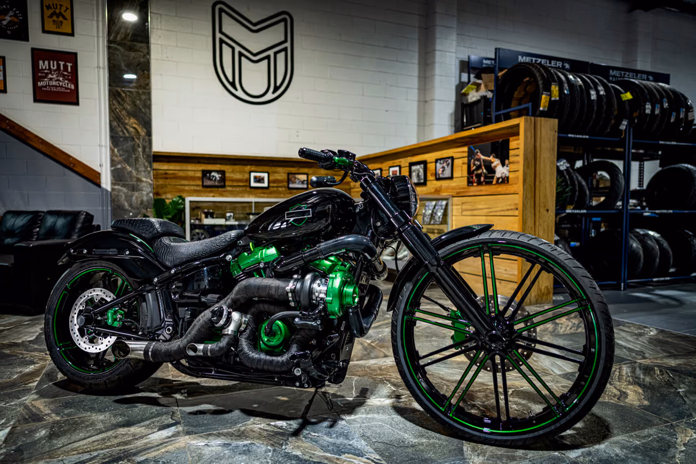 Black and green custom motorcycle with large front wheel parked indoors on stone floor.