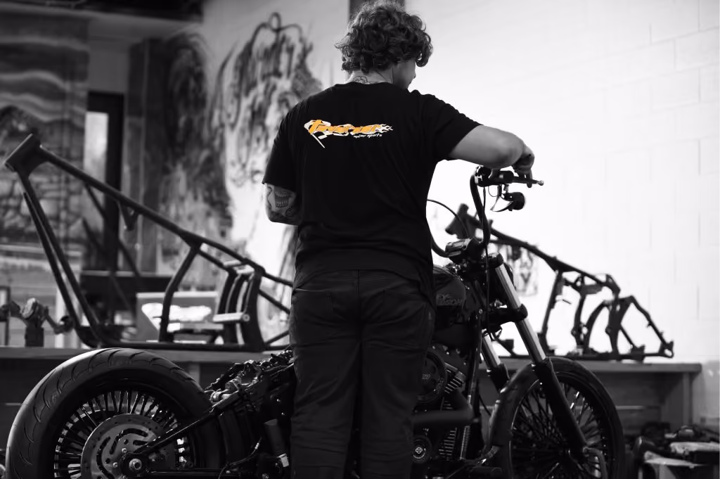 Man working on a motorcycle inside a workshop with bike frames and graffiti in the background.