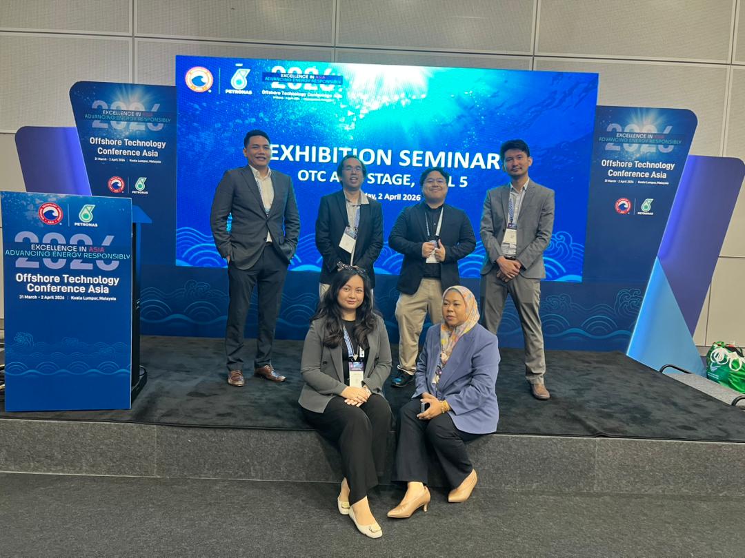 Group of seven diverse people smiling and posing at a trade show booth with EKMS signage.