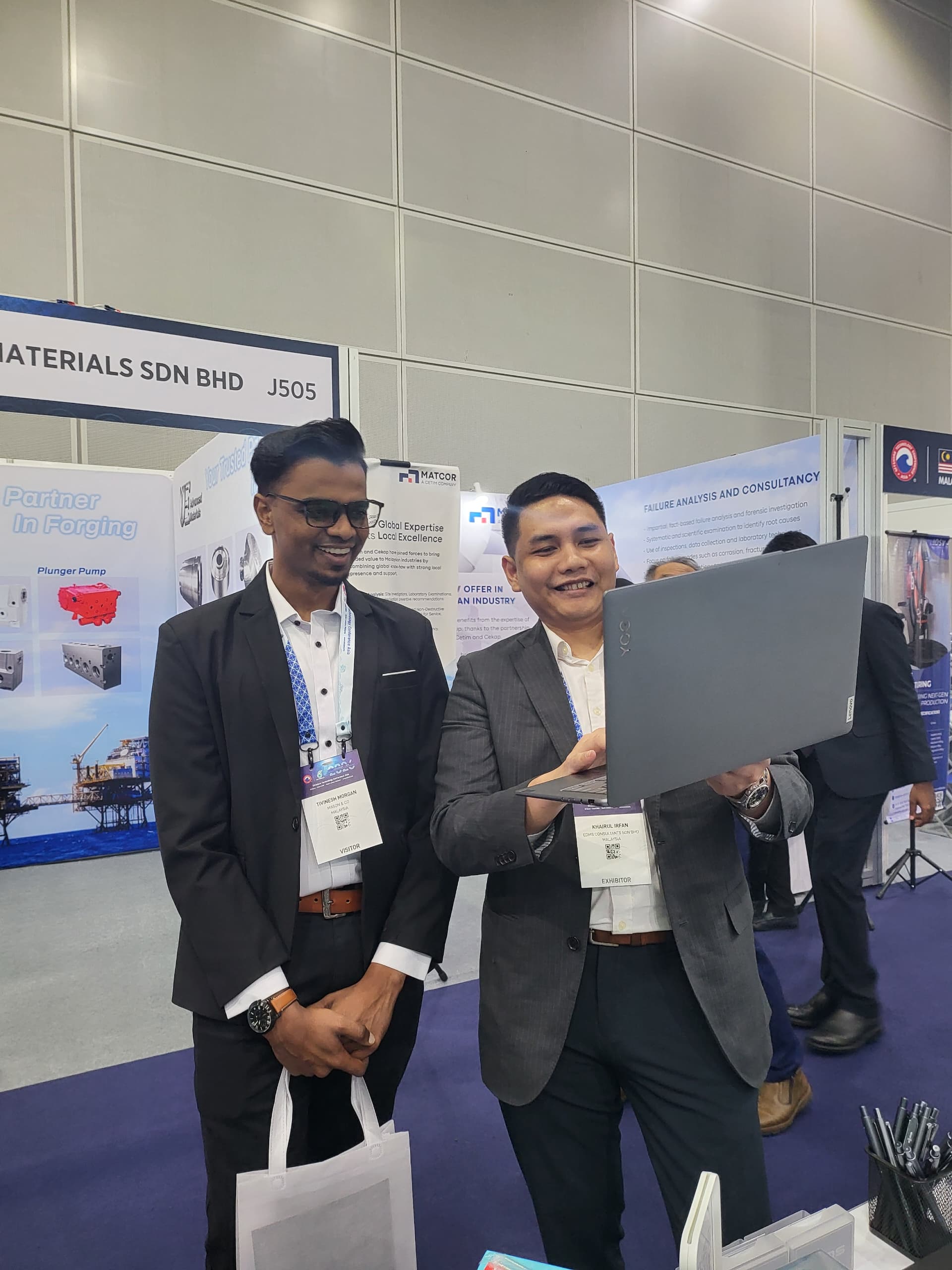 Four business professionals engaged in conversation at an SME Pavilion exhibition booth with banners and a TV screen in the background.