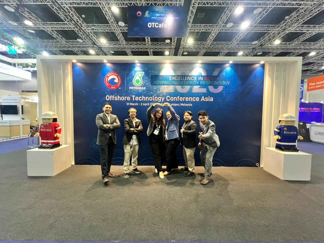 Man in a gray blazer and black pants giving thumbs up at an exhibition booth with banners displaying M-Files and eKMS information on automation and data management.