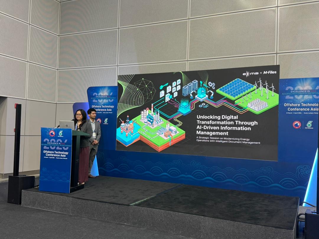 Audience seated in rows watching a speaker presenting on a stage with a digital screen displaying a slide about manual processes and automation.
