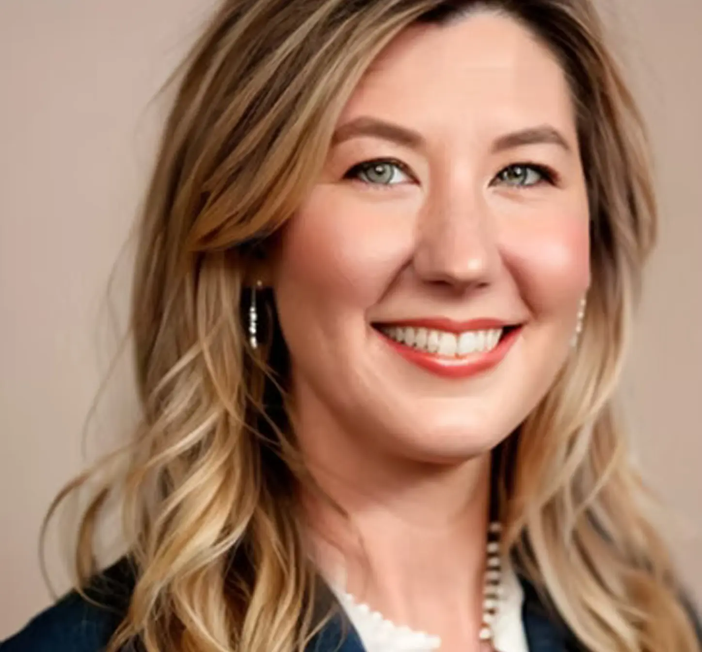 A woman with long hair wearing a blue blazer, smiling confidently while standing against a neutral background.