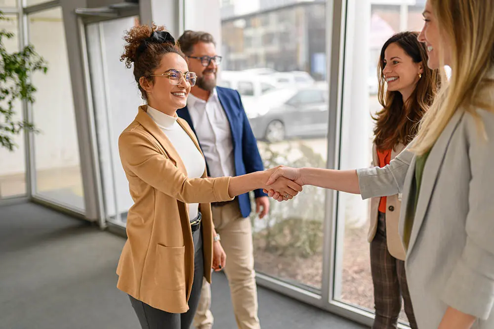 Three business professionals shaking hands in a modern office setting, symbolizing a successful partnership or agreement.