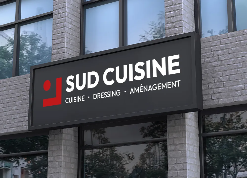 Enseigne noire sur un bâtiment avec texte blanc Sud Cuisine, spécialisé en cuisine, dressing et aménagement, avec un logo rouge à gauche.