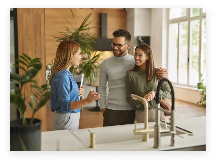 Un couple souriant rencontre une femme pour une visite dans une cuisine moderne et lumineuse.