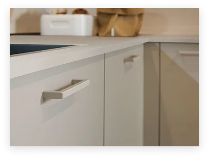 Plan de travail d'angle avec des portes d'armoire de cuisine grises et des poignées métalliques rectangulaires.