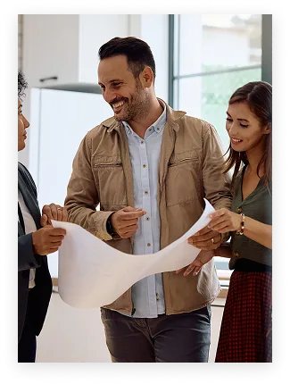 Trois collègues debout discutant autour d'un plan ou d'un projet dans un bureau lumineux.