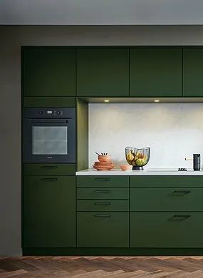 Cuisine moderne avec armoires vert foncé, four encastré, comptoir blanc, bols en terre cuite et corbeille à fruits.