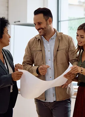 Trois collègues souriants discutant d'un grand document dans un bureau lumineux.