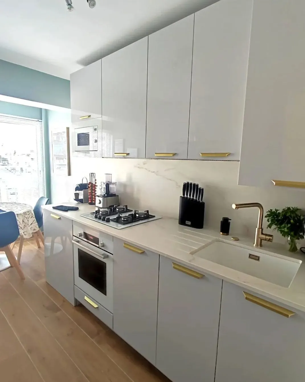 Cuisine moderne avec placards blancs, plaque de cuisson à gaz, four encastré, évier blanc avec robinet doré et un ensemble de couteaux.