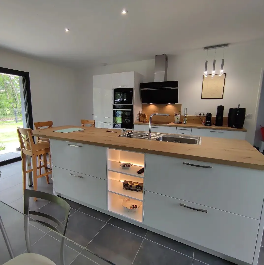 Cuisine moderne avec un grand îlot central en bois clair, siège en bois et électroménagers intégrés.