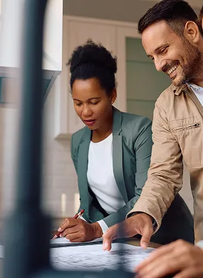 Deux collègues, un homme souriant et une femme concentrée, collaborent en examinant des documents sur une table.
