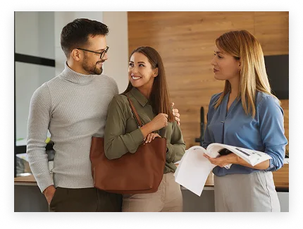 Un couple souriant parle avec une conseillère tenant un magazine dans un bureau moderne.