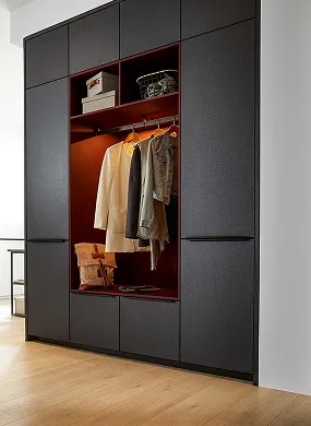 Armoire noire avec section centrale ouverte contenant manteau beige, vestes, chapeaux, sacs et parquet clair.
