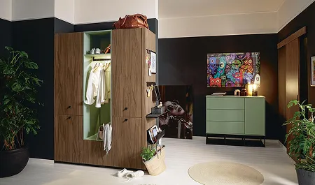 Coin dressing avec penderie en bois ouverte, commode verte, plantes d'intérieur, et tableau coloré sur un mur sombre.