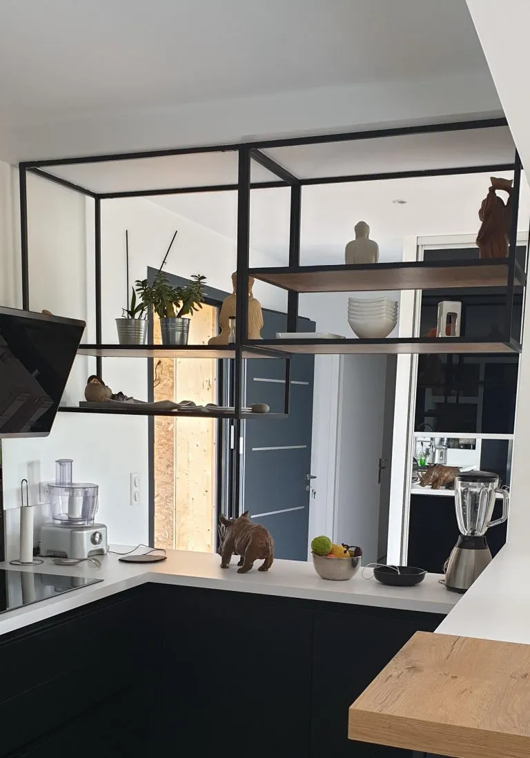 Cuisine moderne avec plans de travail blancs, étagères suspendues, divers objets décoratifs et un chat brun debout sur le comptoir.