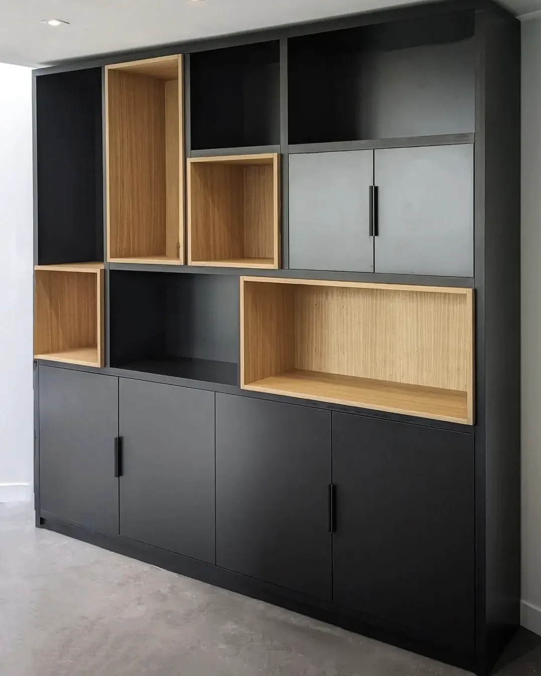 Bibliothèque moderne noire avec étagères ouvertes en bois clair et portes fermées.