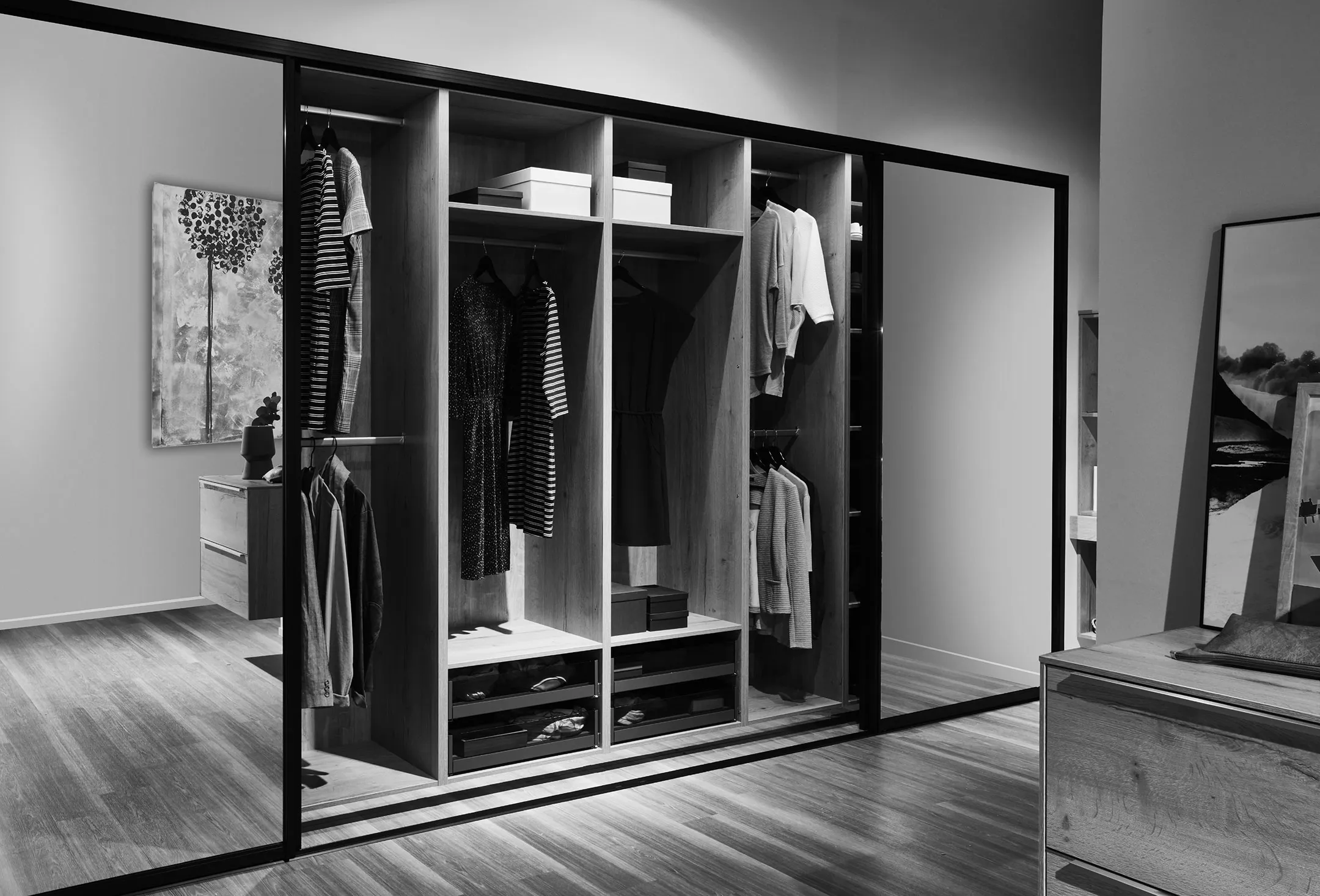 Dressing moderne avec portes coulissantes en verre, vêtements suspendus et tiroirs en bois clair.