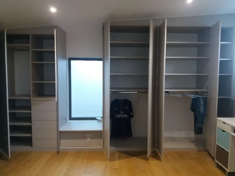 Dressing moderne avec placards ouverts, un maillot de football suspendu et quelques vêtements accrochés, sol en bois clair.