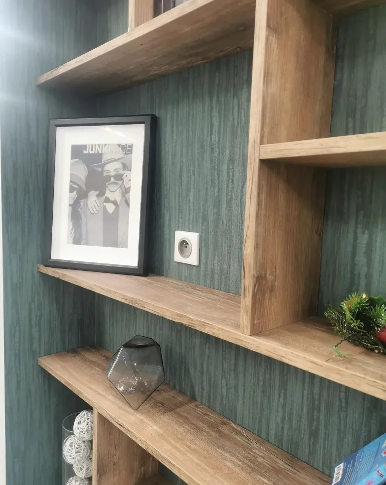 Étagères en bois fixées sur un mur vert avec un cadre photo, un vase en verre et des décorations.