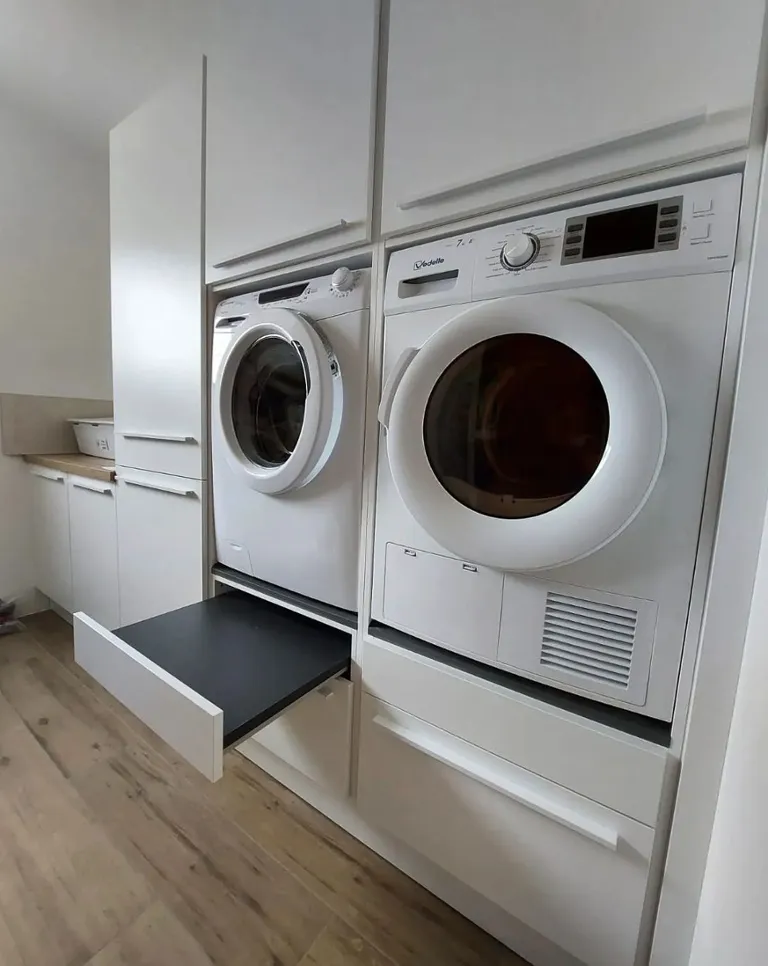 Buanderie moderne avec lave-linge et sèche-linge encastrés dans des armoires blanches, et un plateau coulissant noir entre les deux appareils.