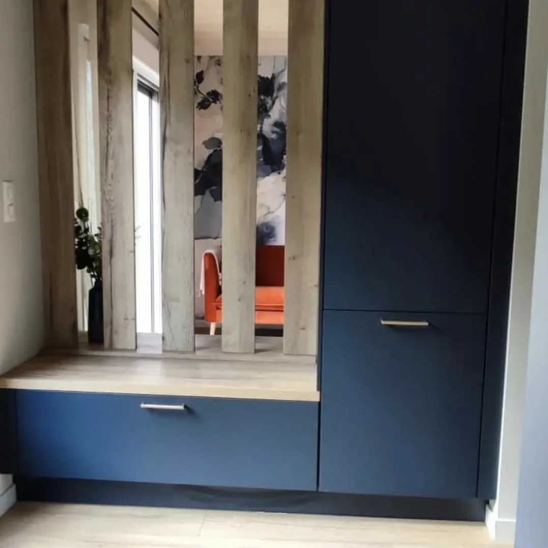 Entrée moderne avec meuble de rangement bleu foncé, banquette en bois clair et parois verticales en bois, reflétant un fauteuil orange et un mur décoré.