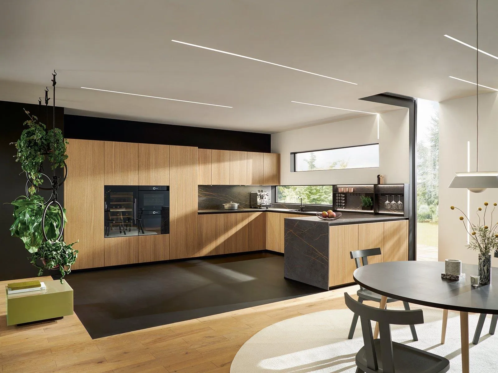 Cuisine moderne avec armoires en bois clair, plan de travail gris foncé et grandes fenêtres.