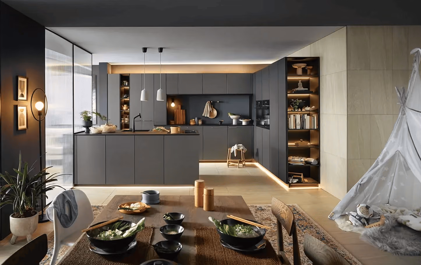 Cuisine moderne grise avec éclairage LED, table en bois dressée et tente pour enfants dans le salon.