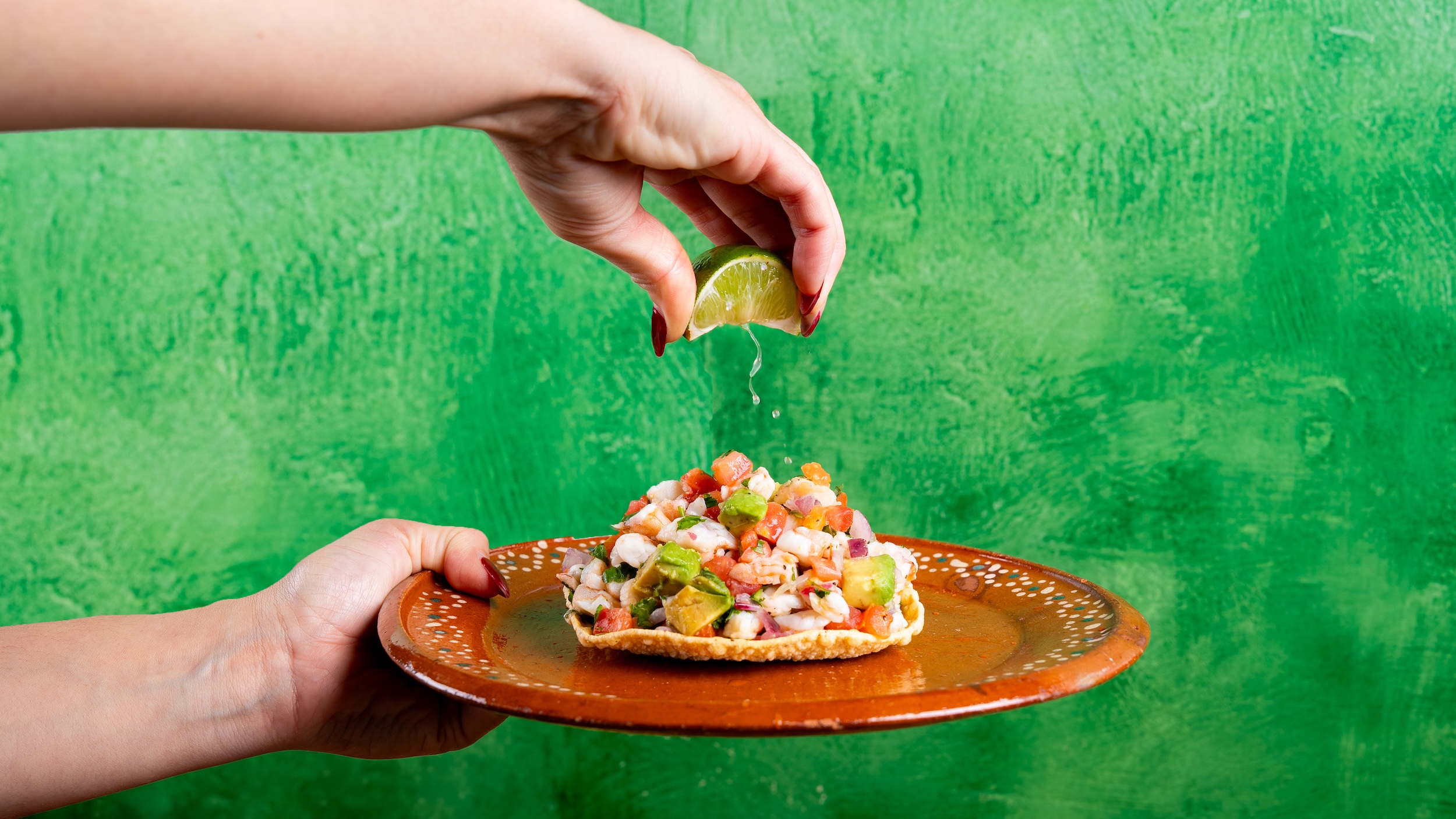 Skillet of melted cheese topped with diced tomatoes and chorizo with a hand holding a toasted tortilla chip and a fork lifting melted cheese.