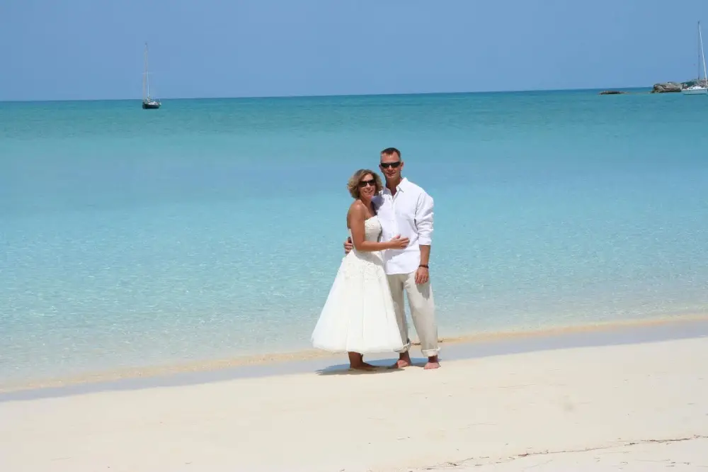 Couple in wedding attire on a white-sand beach beside turquoise water
