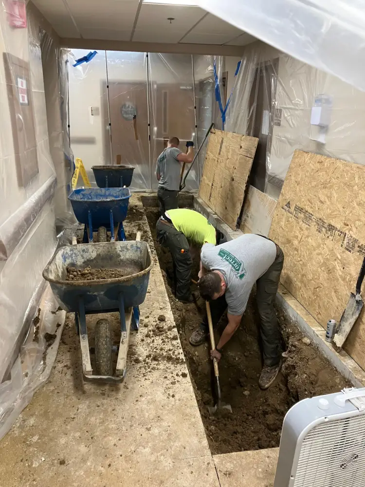 Korrect crew excavating a trench through an interior floor to reach a buried drain line