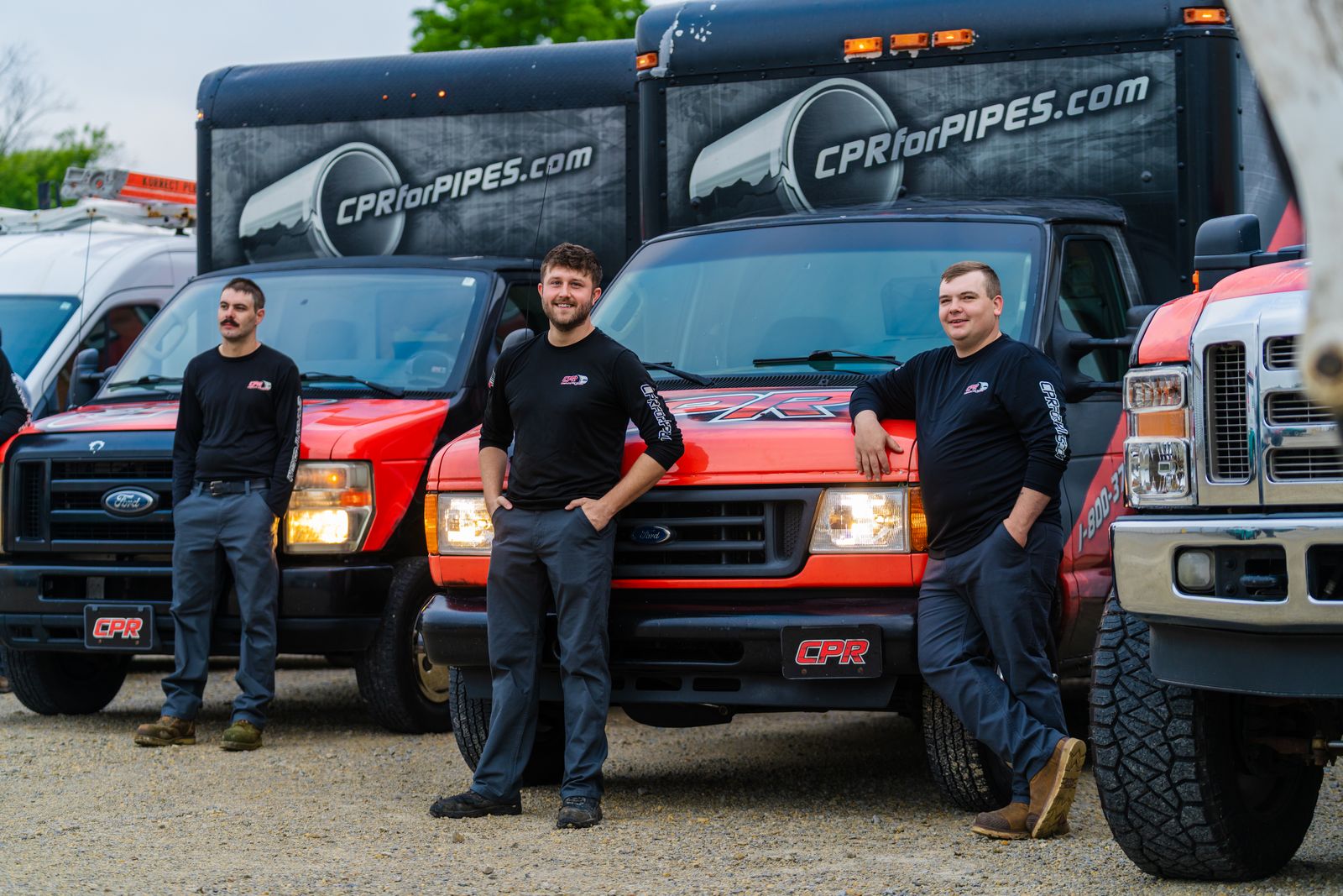Three technicians in black uniforms in front of red CPRforPIPES.com pipe-repair trucks