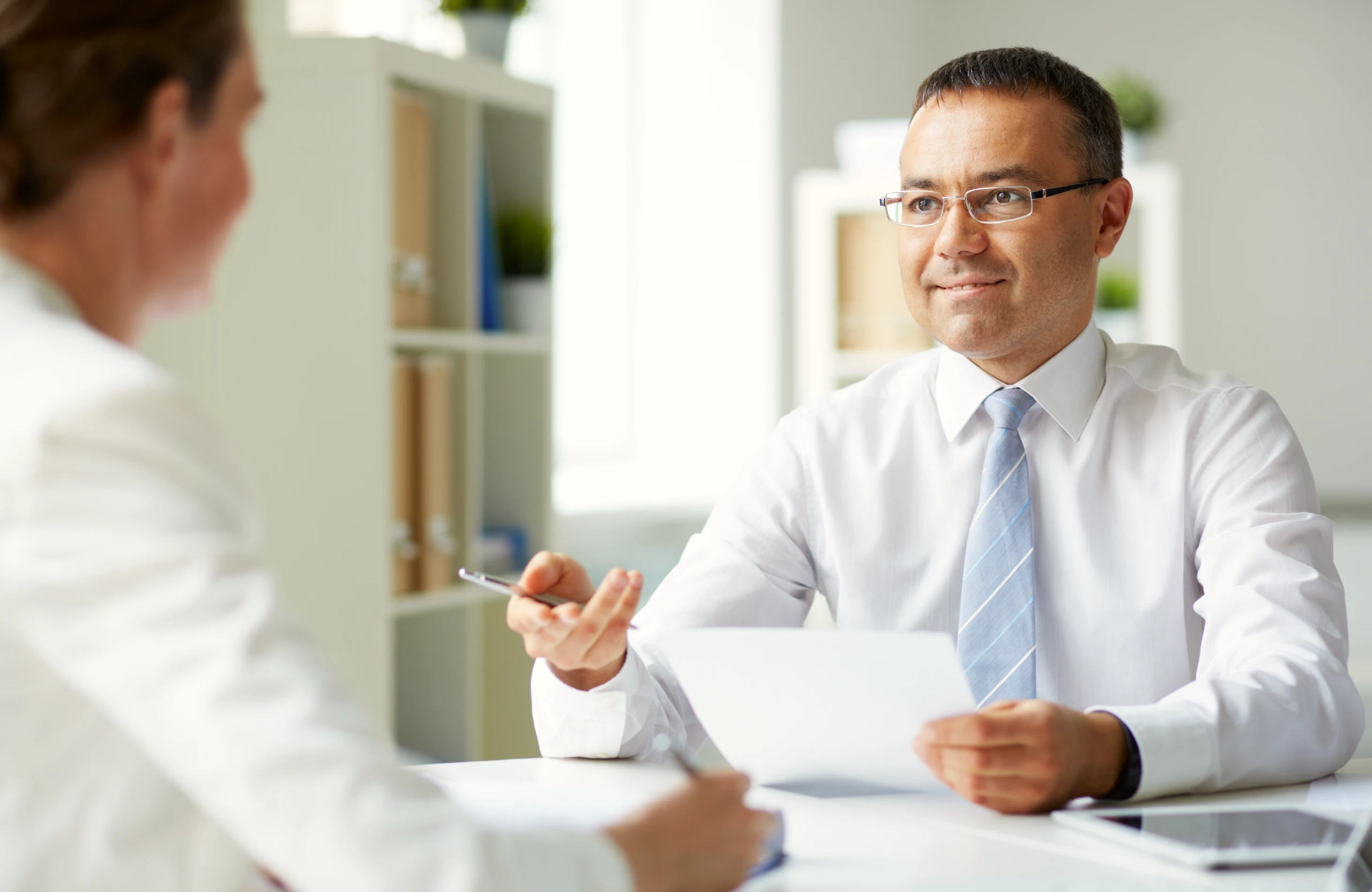 Smiling woman in orange sweater using tablet with stylus while sitting at a table with documents and notebook.