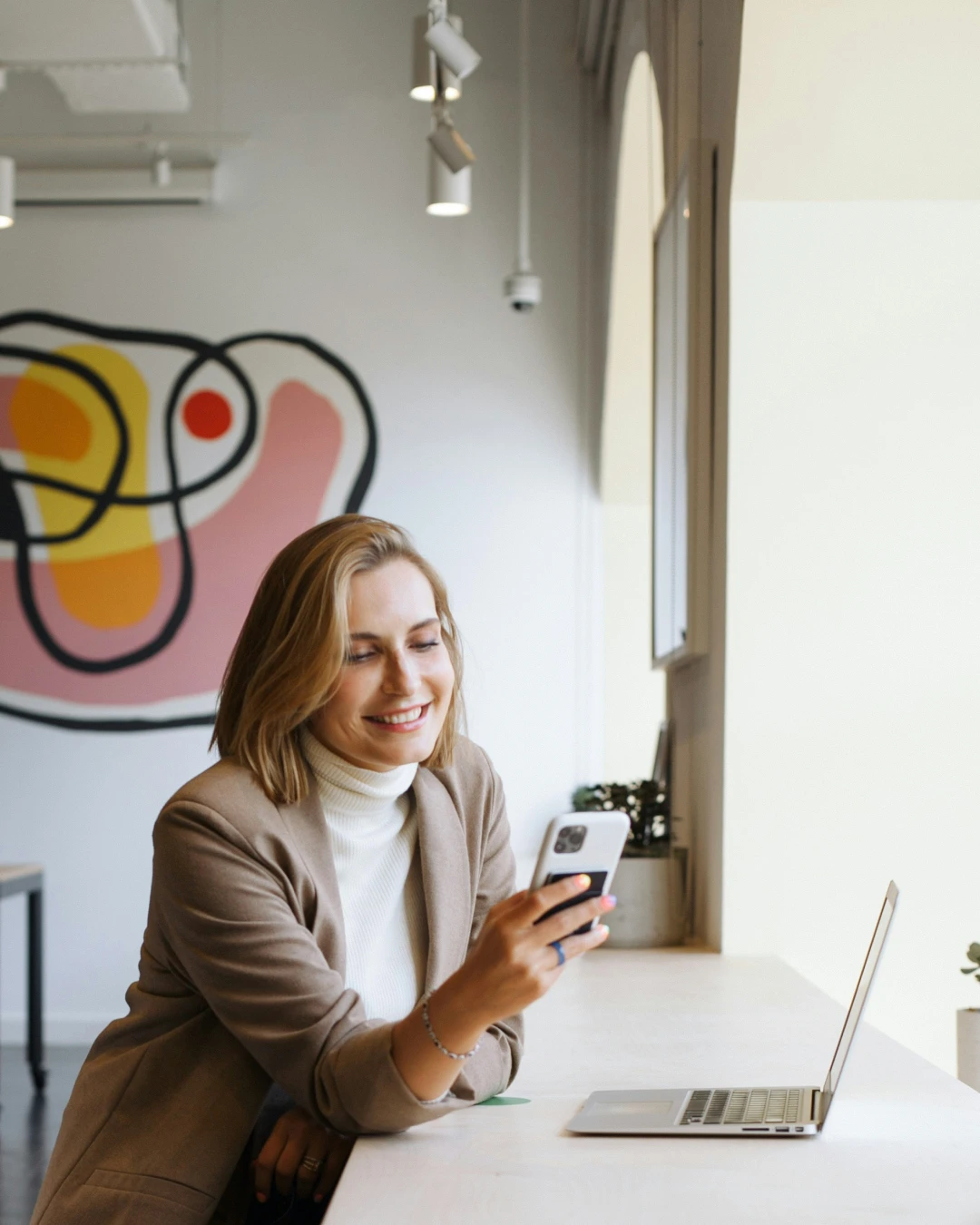 Woman working at a desk with a laptop and smartphone, representing a social media manager managing business communications.