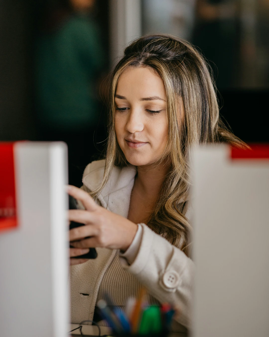 Customer Service Specialist using a smartphone while working at a desk in a modern office.