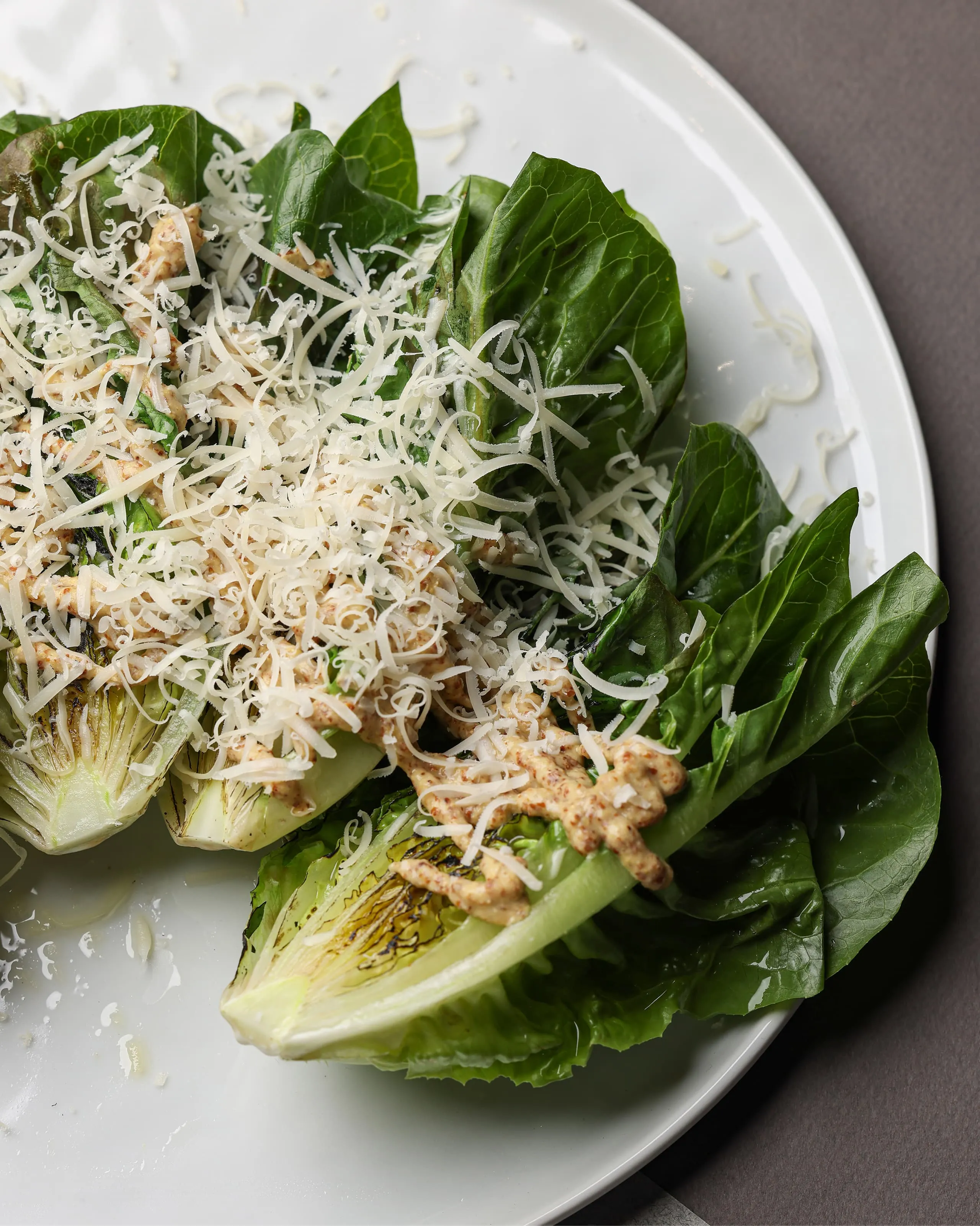 Grilled romaine lettuce halves topped with grated cheese and creamy dressing on a white plate.