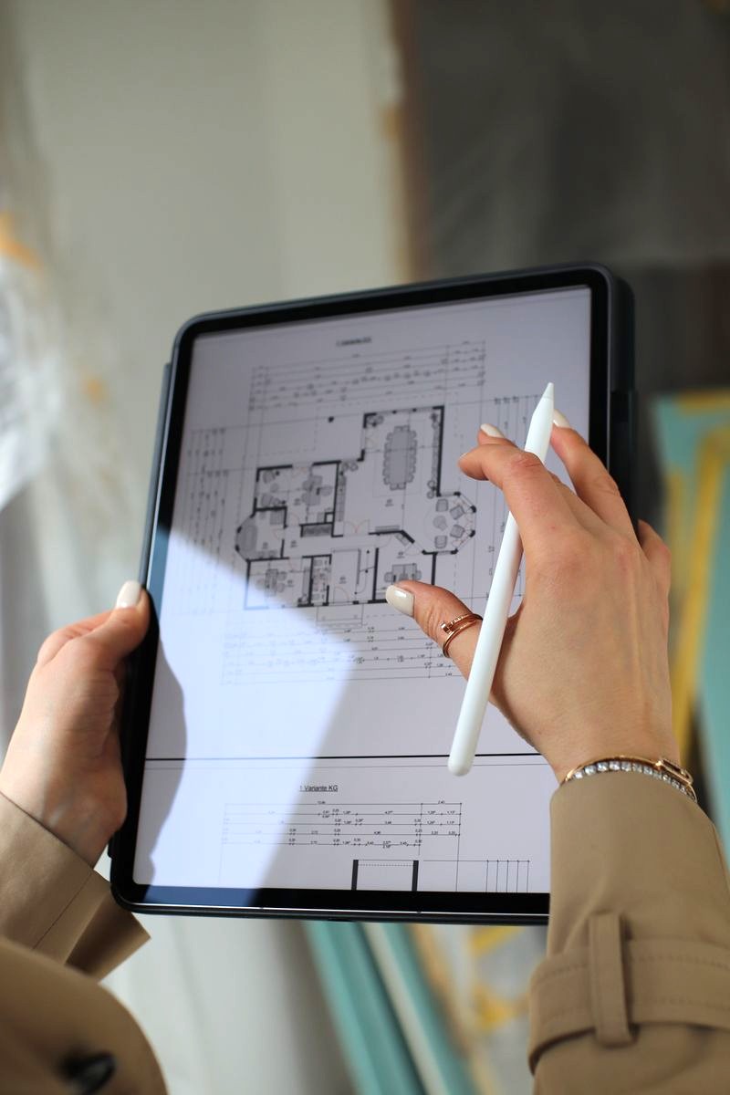 Hands holding a tablet displaying a digital architectural floor plan, with a white stylus pen poised to draw.