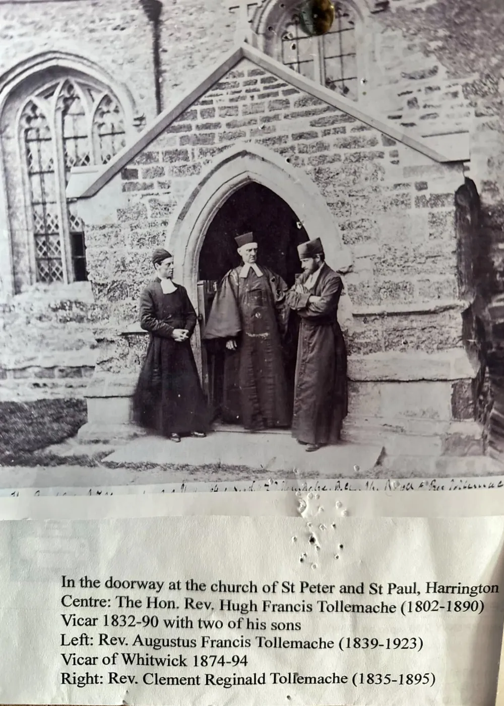Three clergymen standing in the stone doorway of a church with gothic windows in the background.