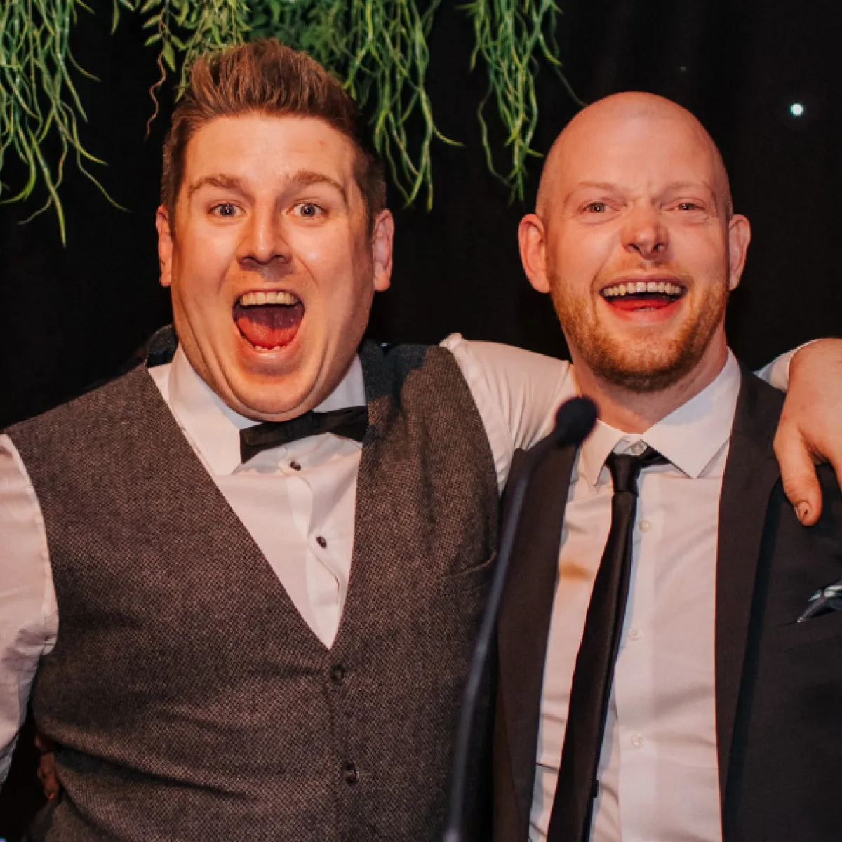 Two men smiling broadly with their arms around each other, dressed in formal attire at an event.
