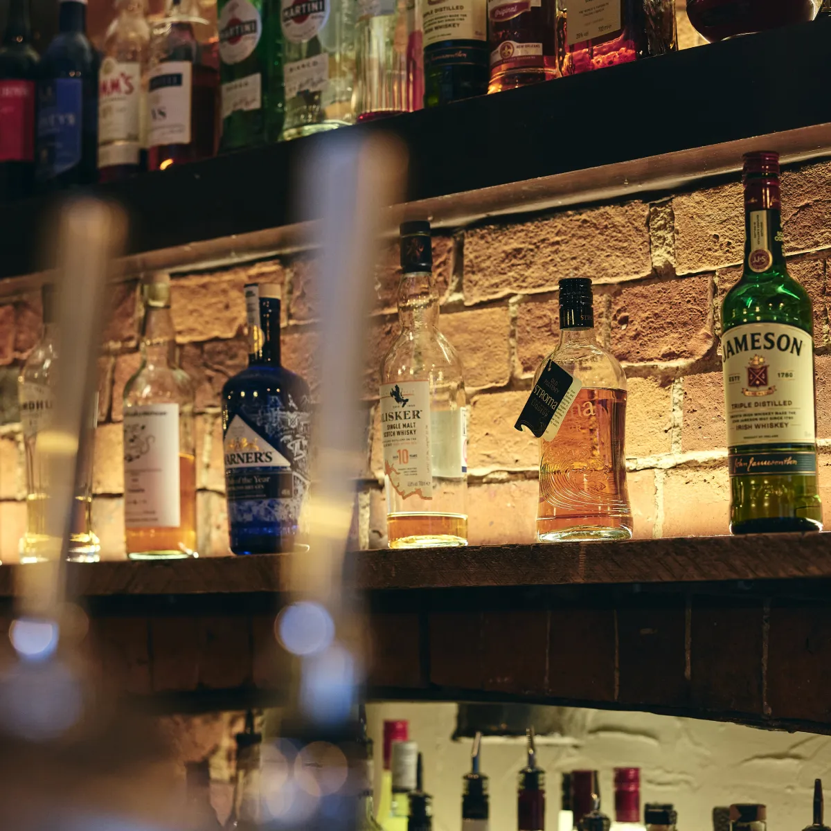 Shelves with various bottles of whiskey and liquor against a brick wall in a dimly lit bar.