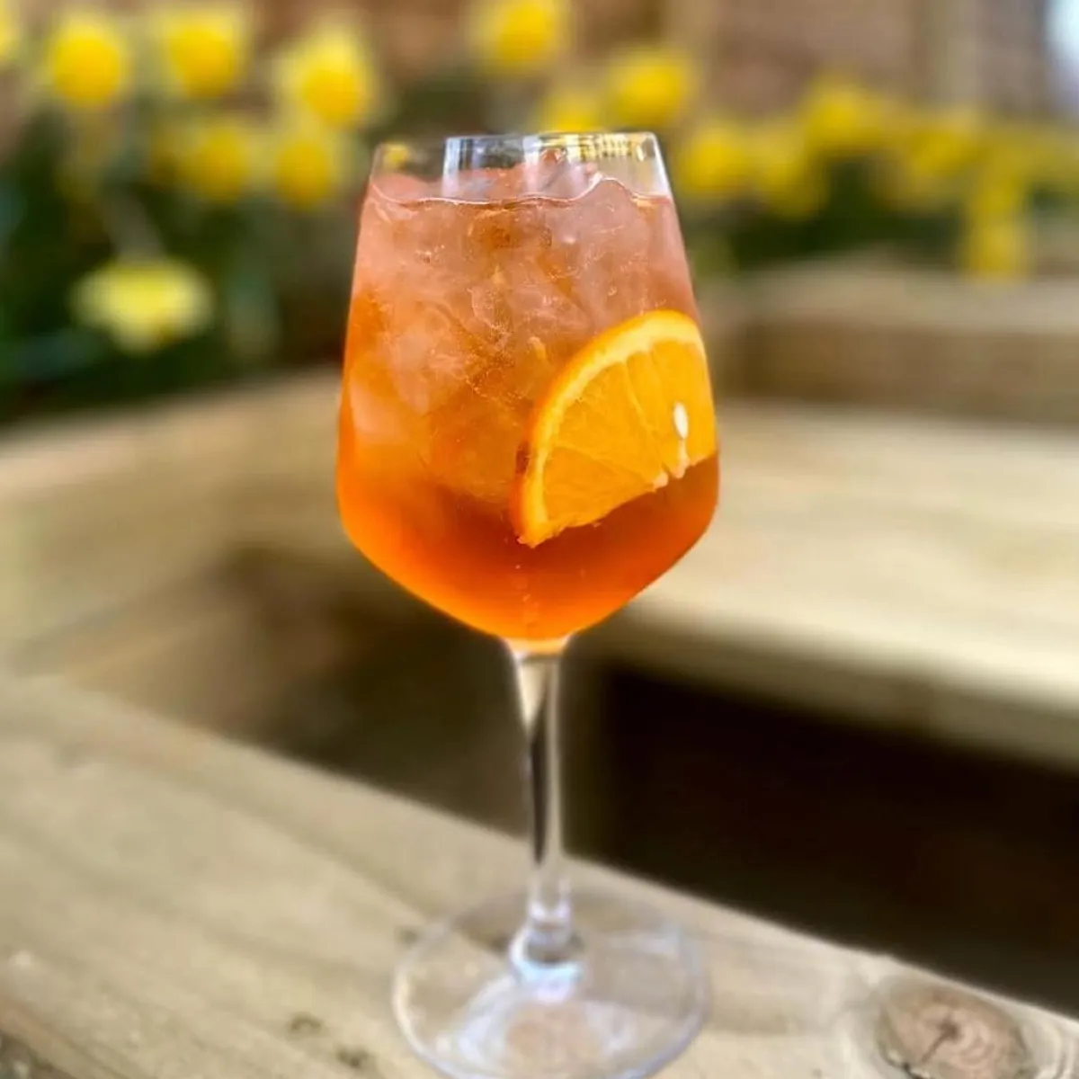 Orange-colored iced cocktail in a stemmed glass garnished with a slice of orange.