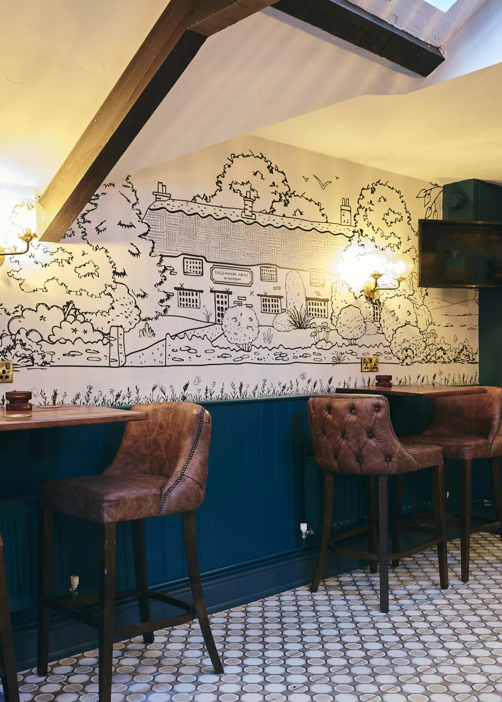 Interior view of a cozy bar area with brown leather bar stools, blue paneling, and a black line-drawing mural of a countryside house on the wall.