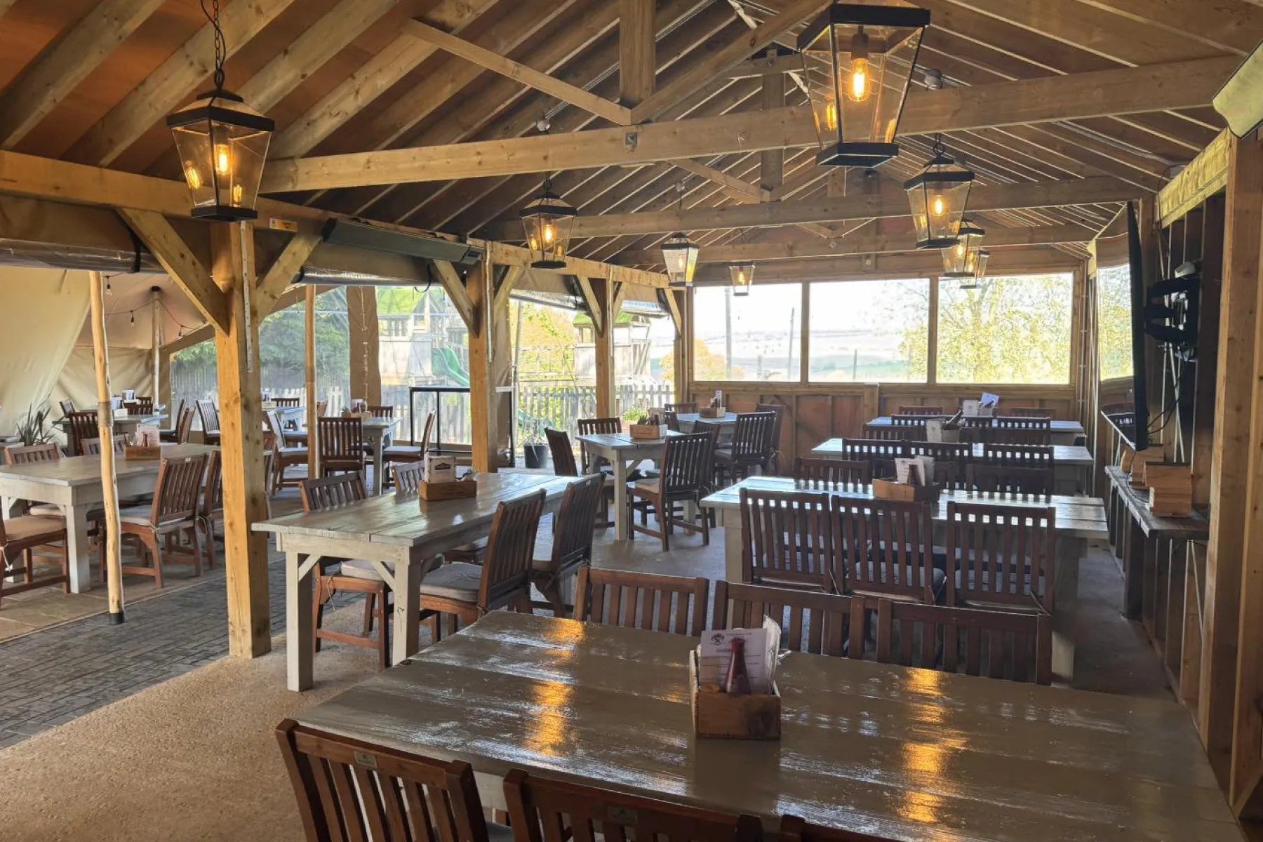 Cozy outdoor covered dining area with wooden tables, chairs, and hanging lantern lights.