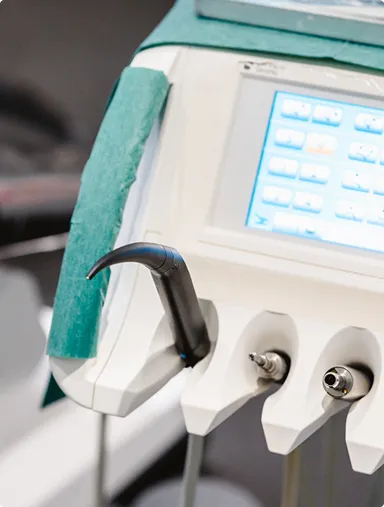 Close-up of a dental ultrasonic scaler attached to a dental unit with control buttons visible on the screen.