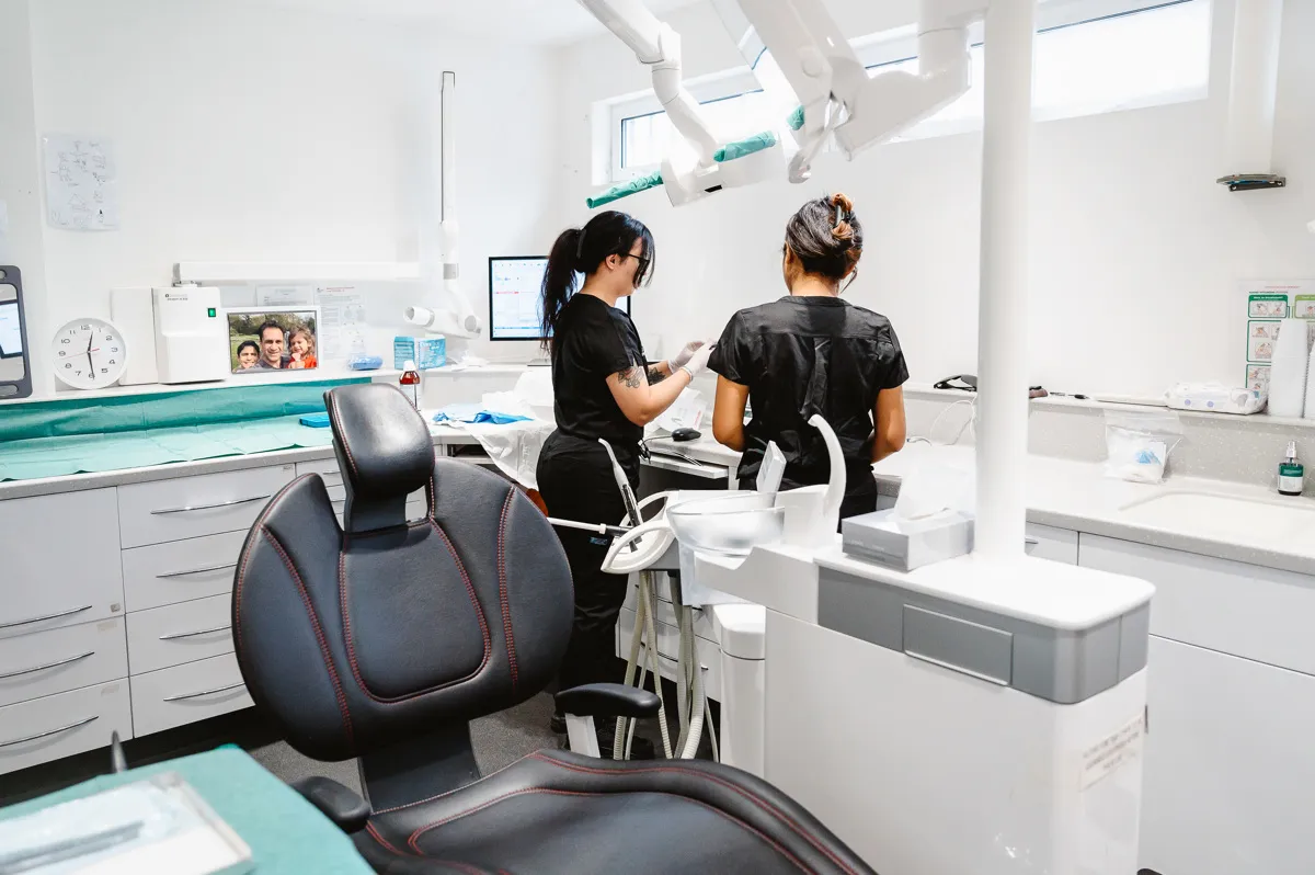 Modern dental clinic with two dental professionals in black scrubs preparing equipment near a dental chair.